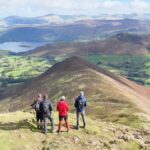 Four walkers looking across a Lake District ridge and valley