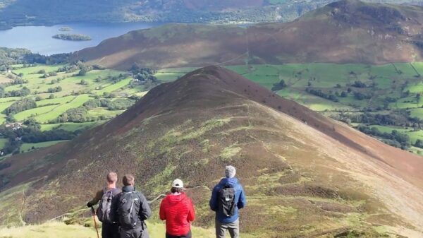 Four walkers looking across a Lake District ridge and valley