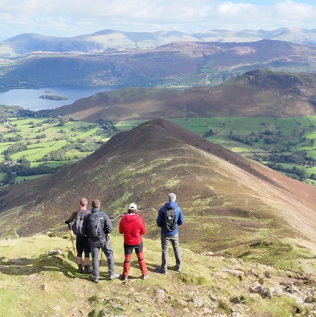 Four walkers looking across a Lake District ridge and valley